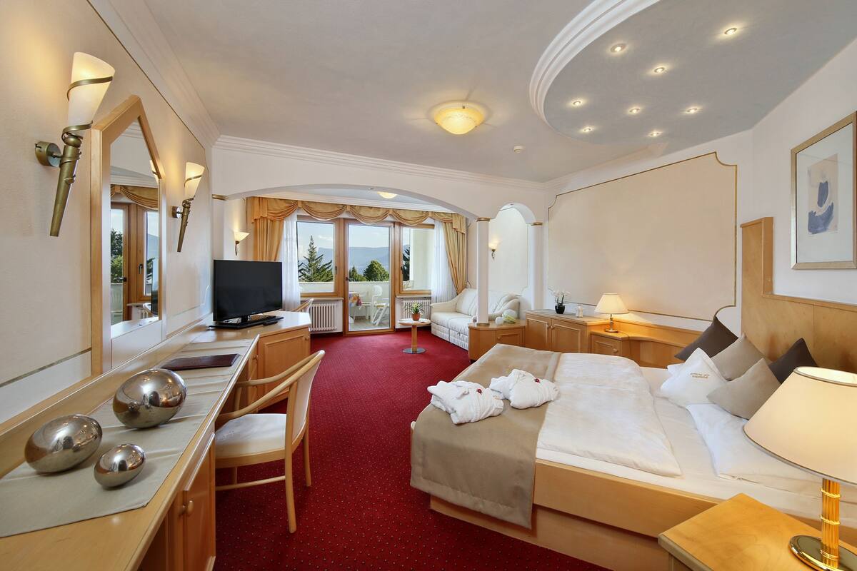 A hotel room with a bed, desk, chair, TV, and a view of the outdoors.