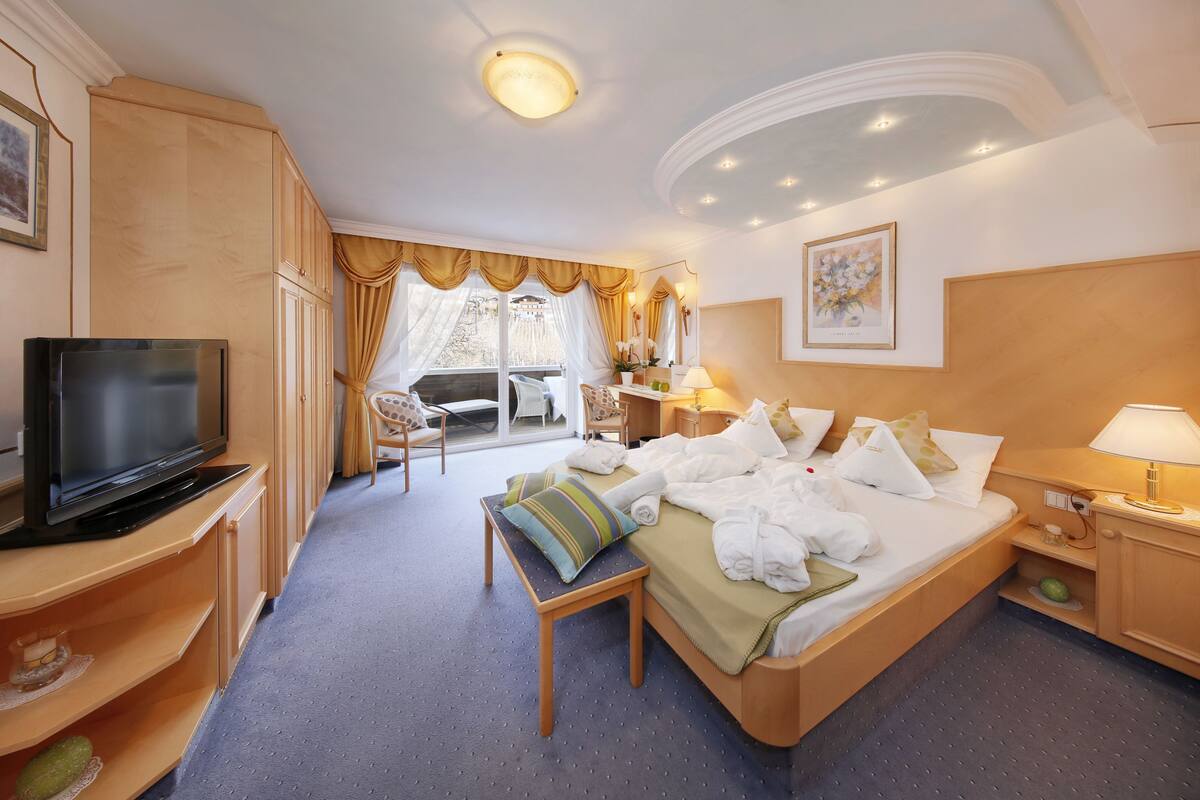 A hotel room with a bed, a TV, a desk, a chair, and a window with curtains.