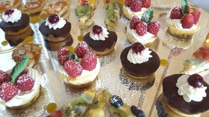 Una variedad de postres en una bandeja, incluyendo pasteles con cobertura de chocolate, crema batida y frutos rojos, además de pasteles con fruta.