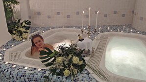 A bathtub with mosaic tiles, candles, and a bouquet of flowers. - Wellness Parc Hotel Ruipacherhof (Tirolo)