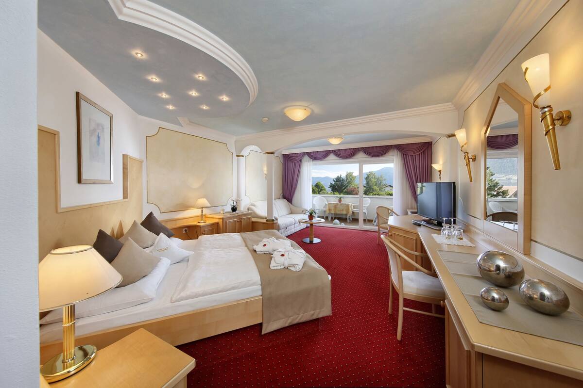 A hotel room with a large bed, a desk, a chair, a TV, and a window with a view.