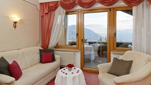 A room with a white sofa, a round table with a vase of red roses, and a view of mountains through a glass door. - Wellness Parc Hotel Ruipacherhof (Tirolo)
