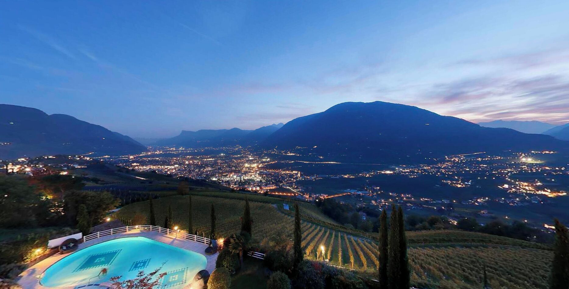 A nighttime view of a city with a mountain in the background and a swimming pool in the foreground.