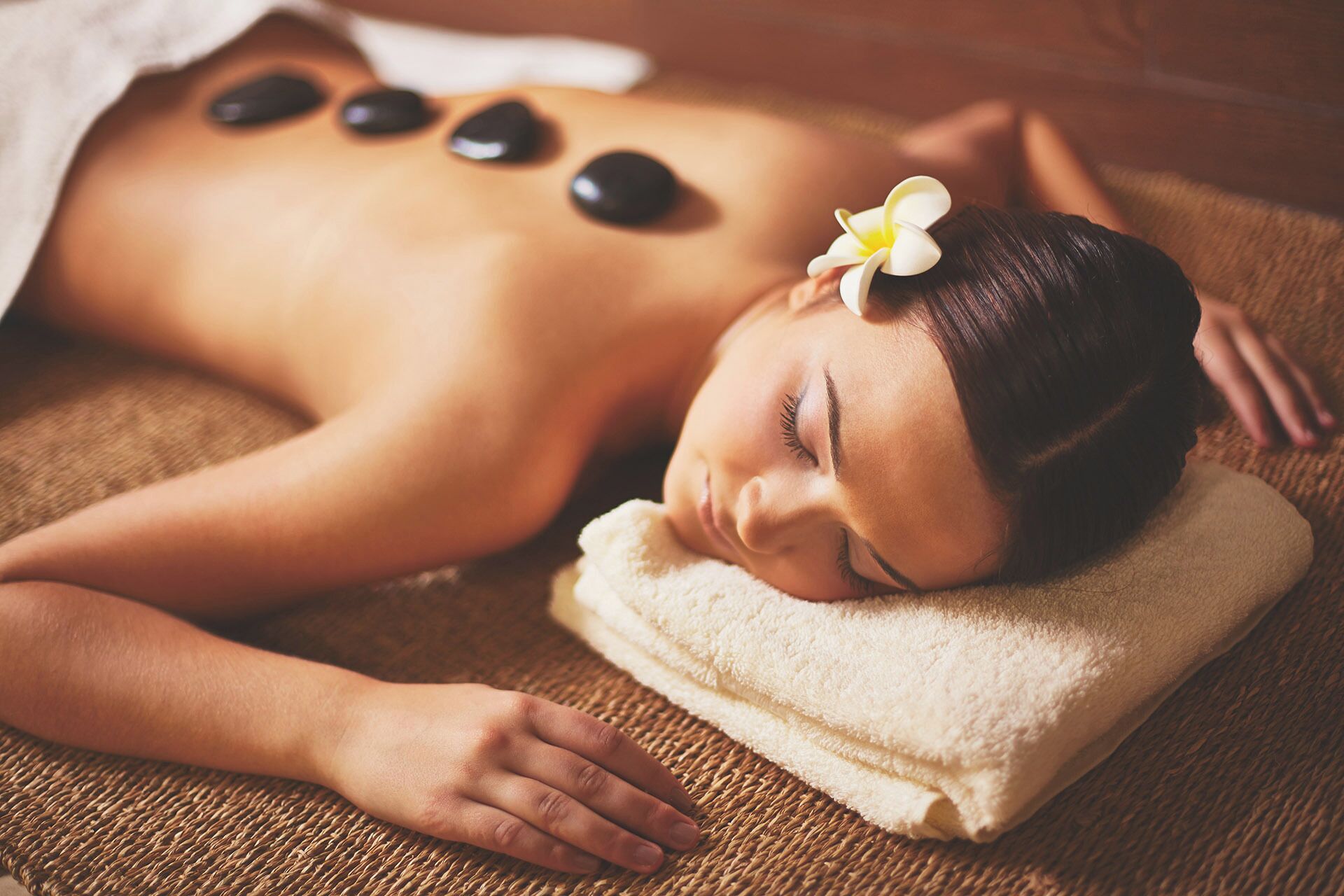 A person receiving a back massage with stones on their back, lying on a textured mat.