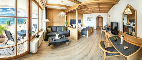 A spacious living area with a large window, wooden flooring, and a cozy seating arrangement including a sofa and a bed.