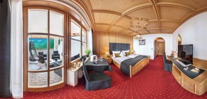 A hotel room with a large window, a bed, a desk, and a TV. - Panorama Vital Hotel Rimmele (Tirolo)