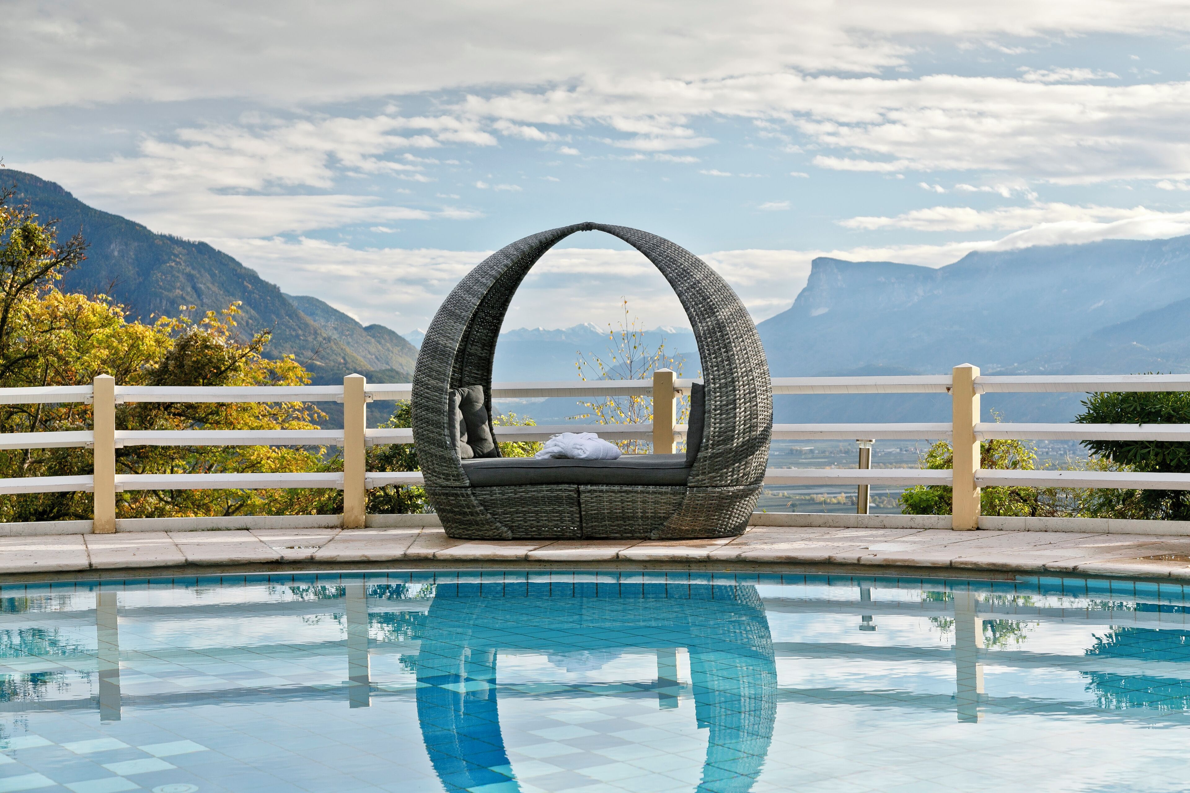 A wicker lounge chair by a pool with a mountain view.