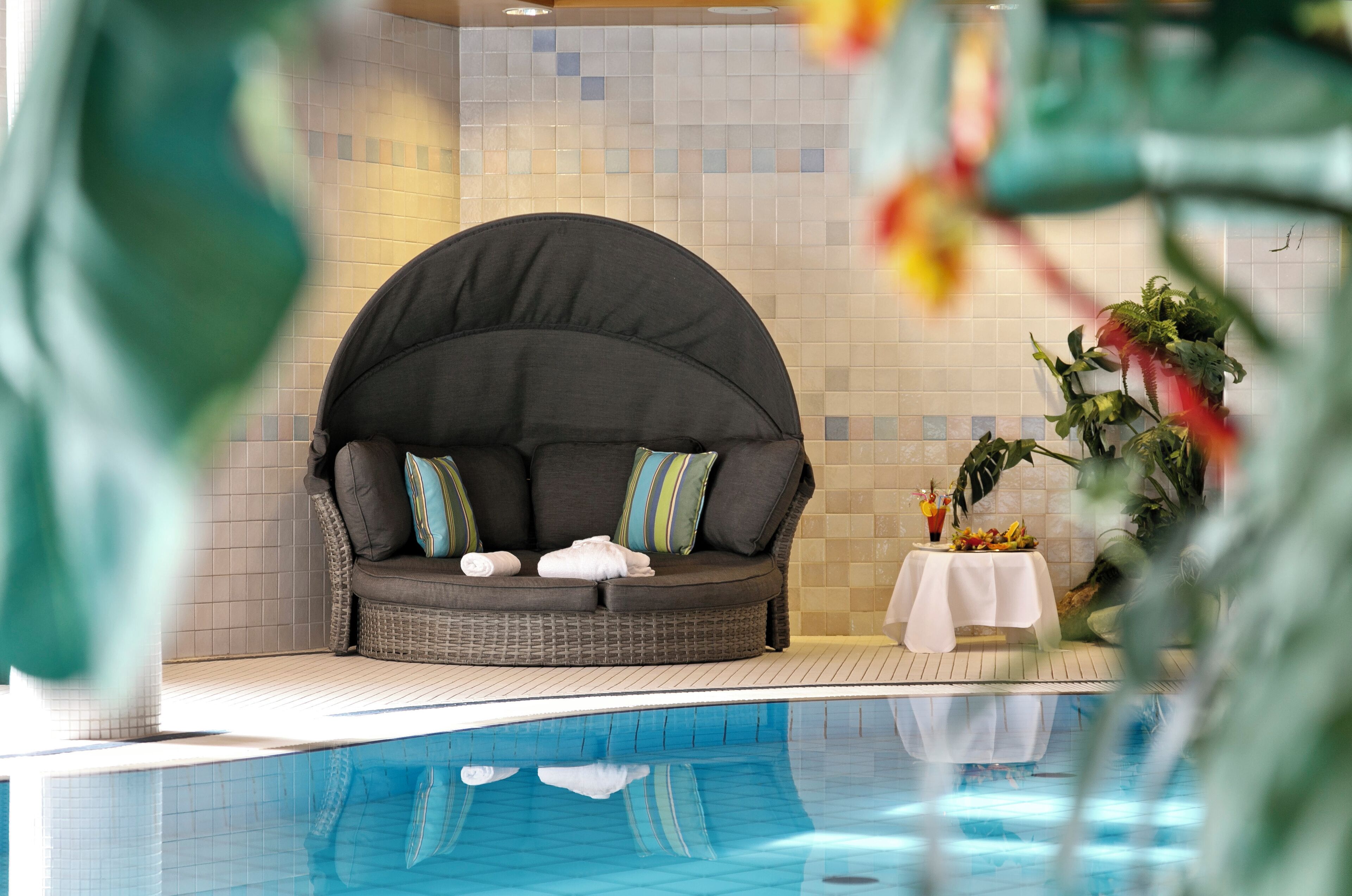 A poolside seating area with a cushioned bench and a small table with a drink and fruit.