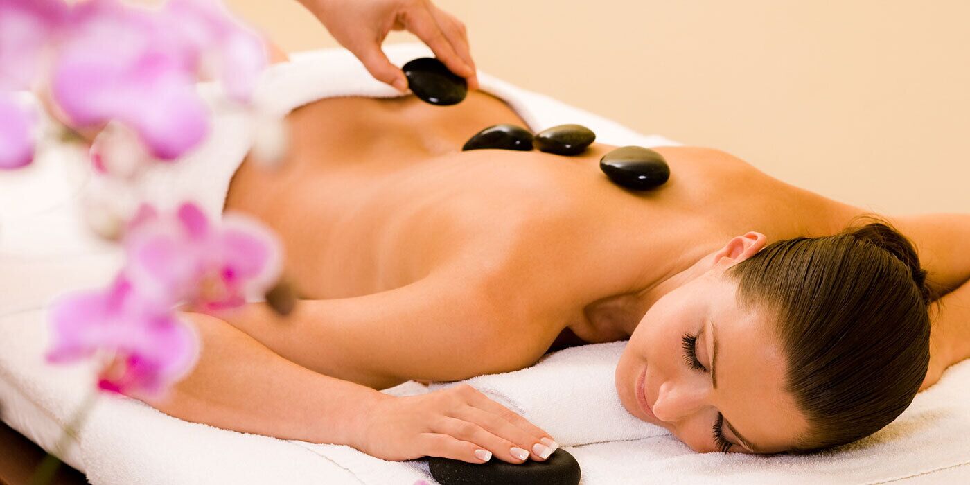 A person receiving a stone massage with black stones placed on their back.