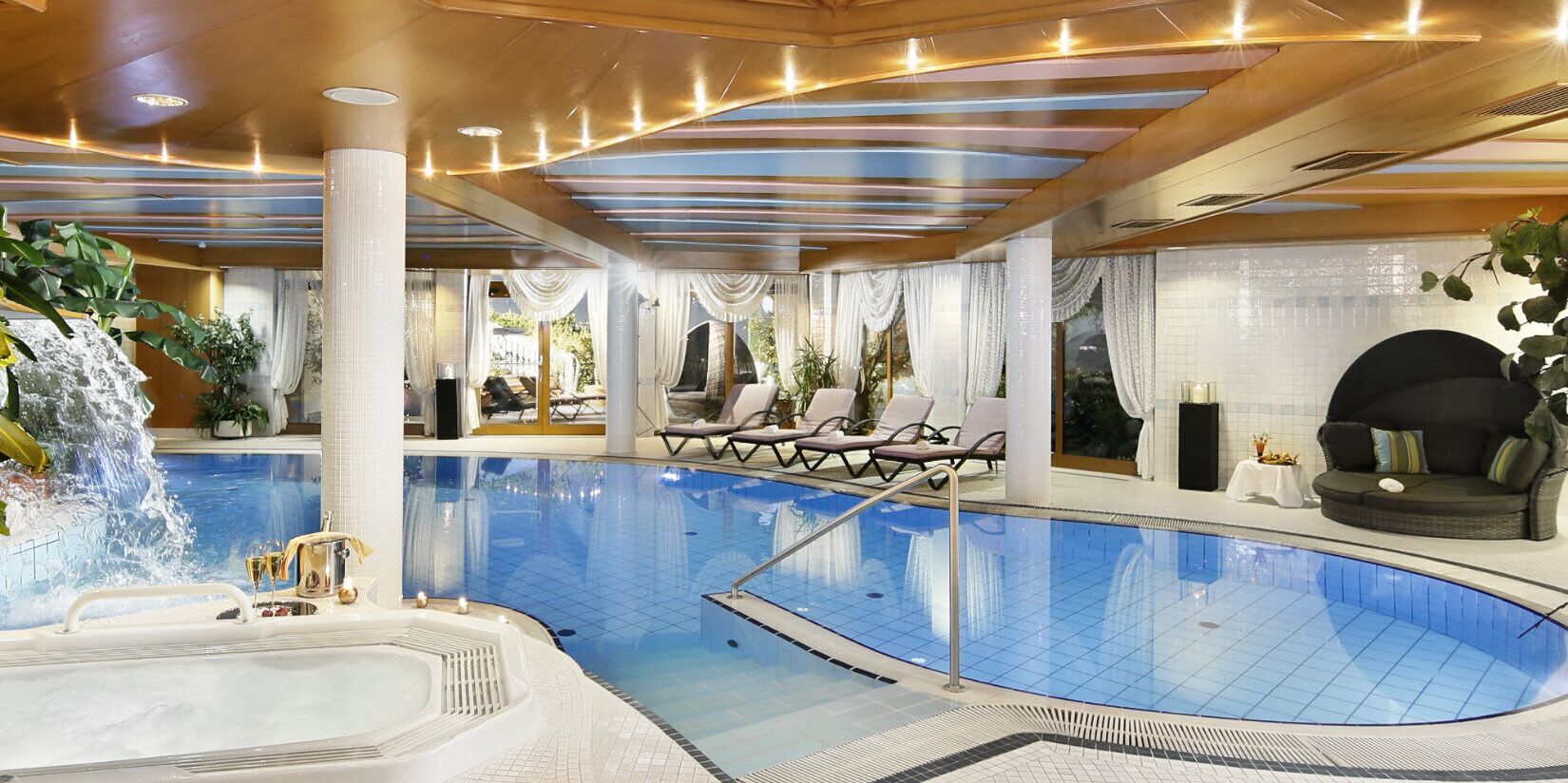 Una gran piscina cubierta con jacuzzi, sillas de descanso y una cascada.