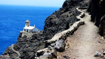 A narrow, rocky path leading to a small white building with a bell tower, overlooking a deep blue sea.