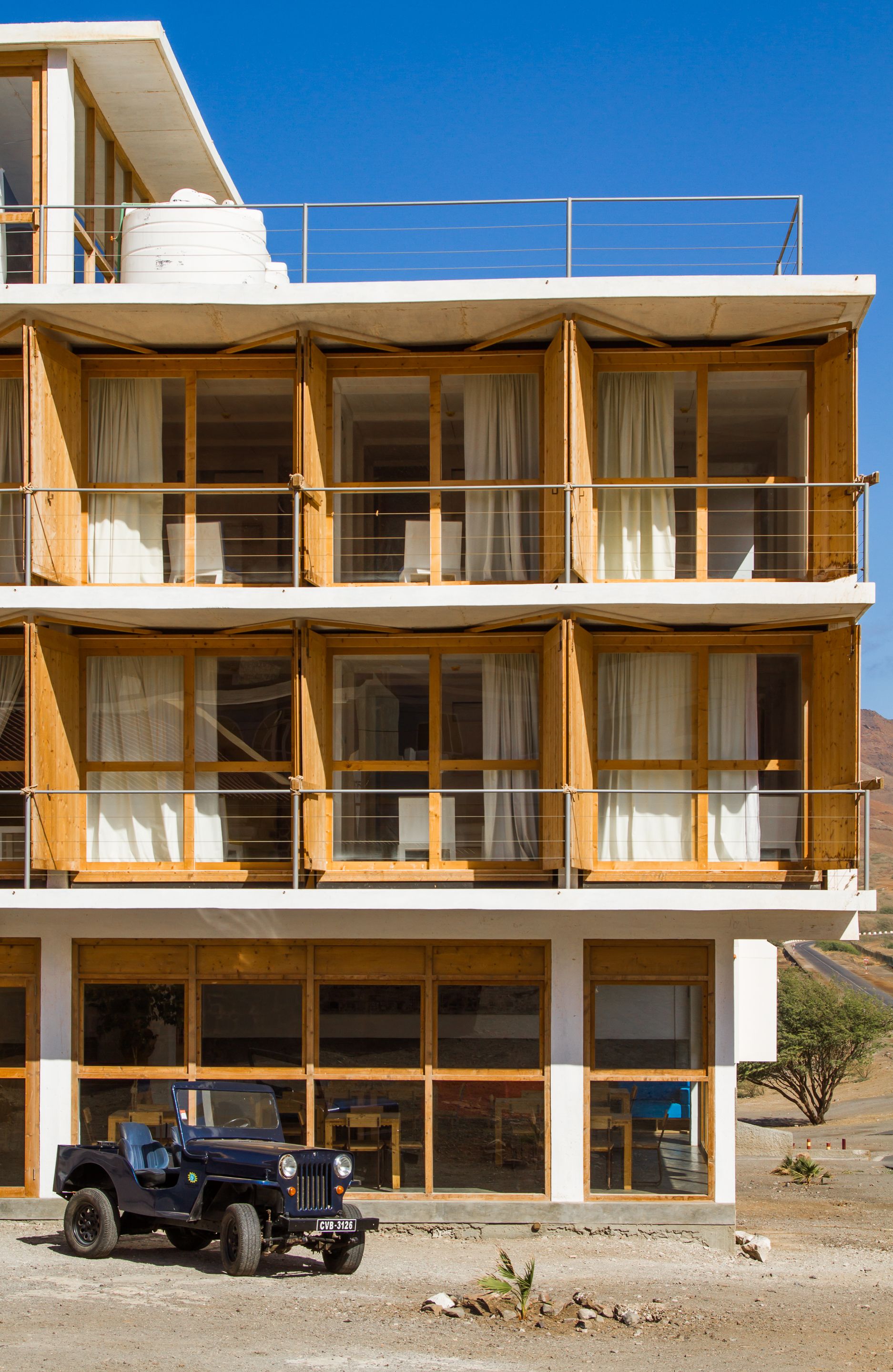 Un immeuble à plusieurs étages doté d’un balcon, de grandes fenêtres et d’un véhicule garé devant.