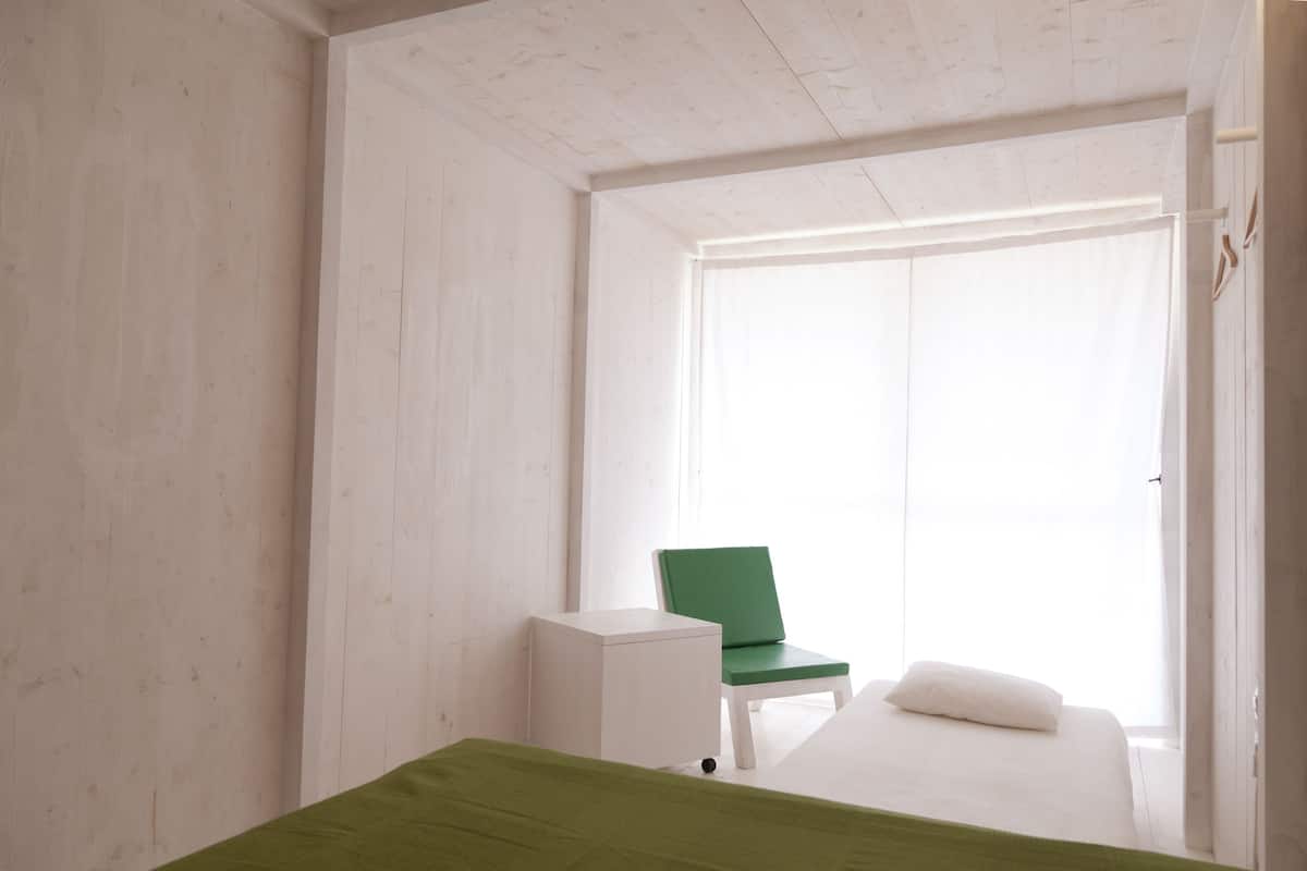 Une chambre avec un lit, un fauteuil vert et une table de chevet blanche.