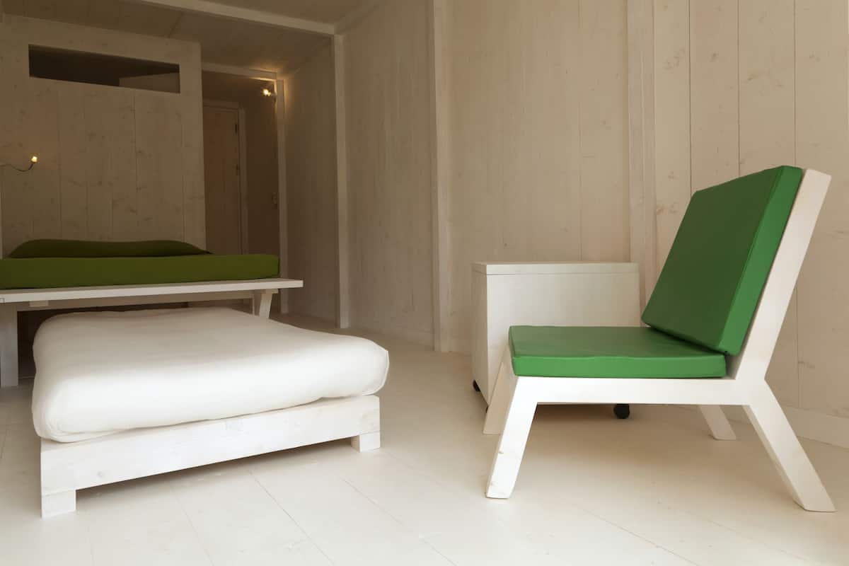 Une pièce minimaliste comprenant un lit, un banc et une chaise.