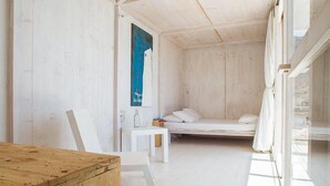 Une pièce au décor minimaliste, avec un plancher en bois, un lit blanc, une petite table blanche et un bureau en bois.