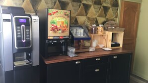 A coffee station with a coffee machine, a beverage dispenser, and a display of coffee cups. - Hotel Victor Hugo (Dijon)