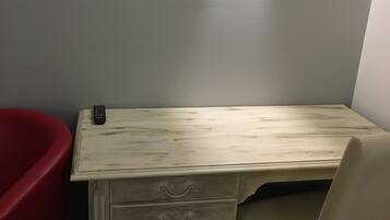 A small, white, wooden desk with two drawers and a red chair. A remote control is on the desk.