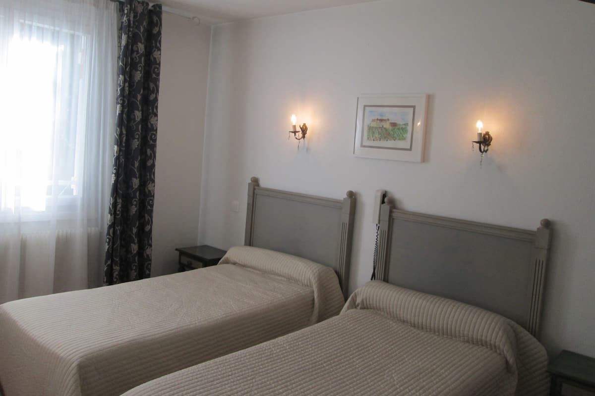 Quarto com duas camas, uma mesa de cabeceira, uma luminária e um quadro na parede.