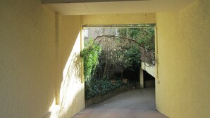 A narrow hallway with a yellow wall, a door at the end, and a view of greenery outside. - Hotel Victor Hugo (Dijon)