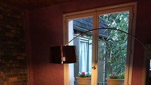 A cozy living room with a sofa, armchair, and a table with a lamp. A window with a view of greenery is visible. - Hotel Victor Hugo (Dijon)