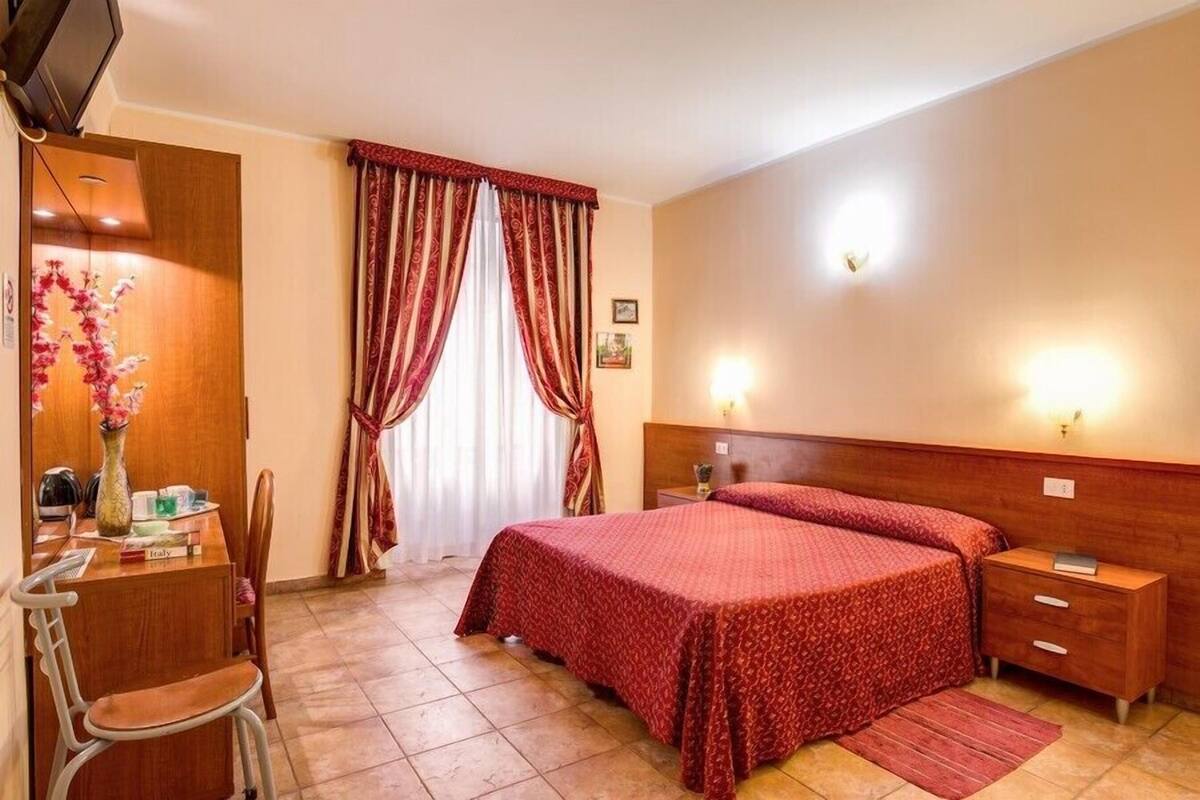Una habitación de hotel con una cama, un escritorio, una silla, una mesita de noche y un televisor.
