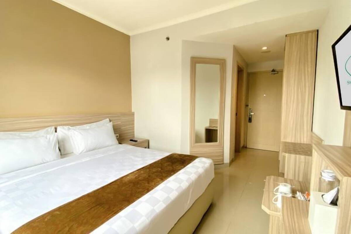 Ein Hotelzimmer mit einem großen Bett, einem Holzkopfende, einem Nachttisch, einem Spiegel und einem Holzschrank.