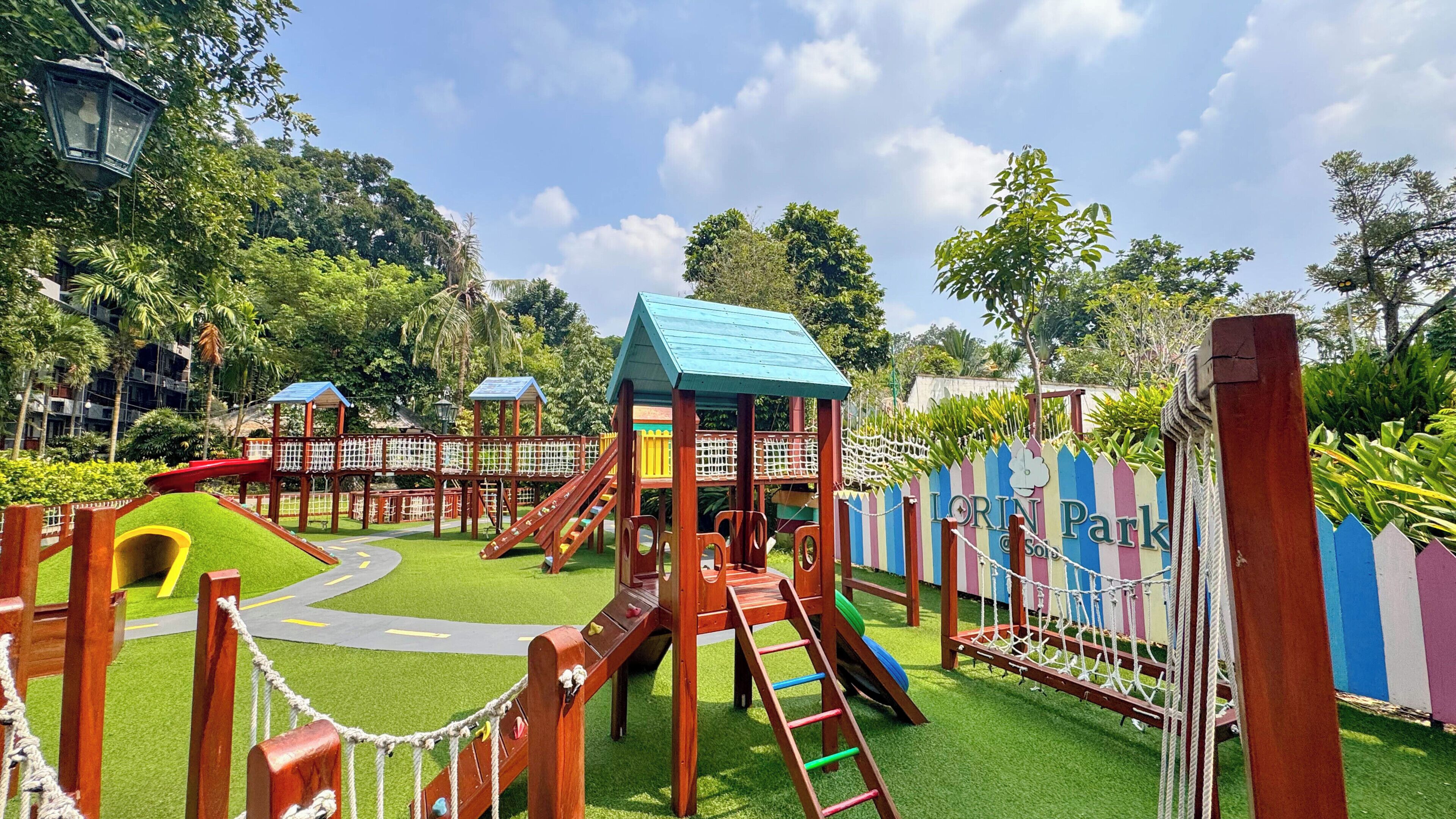 A playground with slides, climbing structures, and a fenced area with a sign reading 'Lorin Park.'