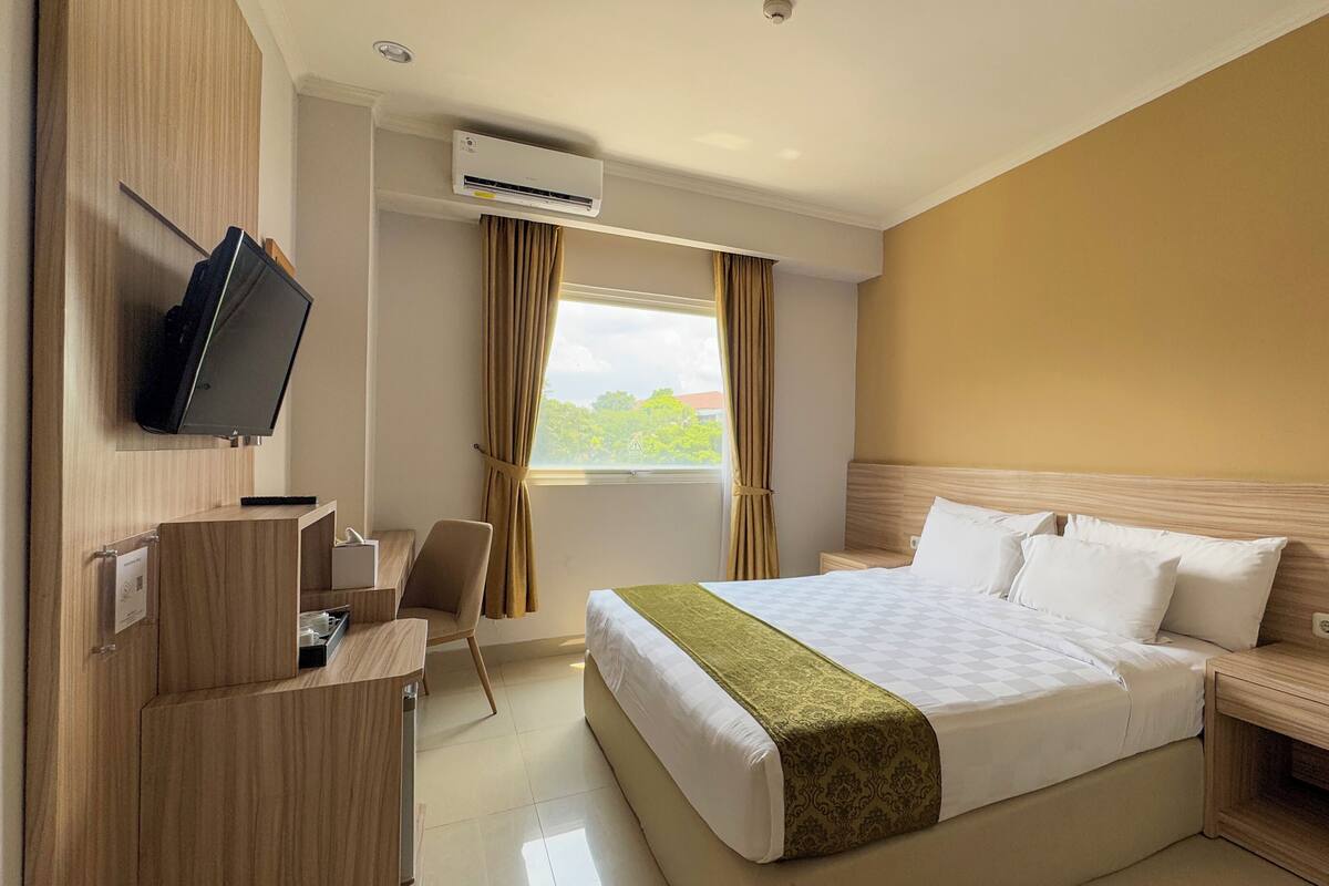 A hotel room with a bed, a desk with a chair, a television, and an air conditioning unit.