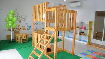 A children's playroom with a wooden playhouse, green carpet, alphabet foam mats, and wooden furniture.
