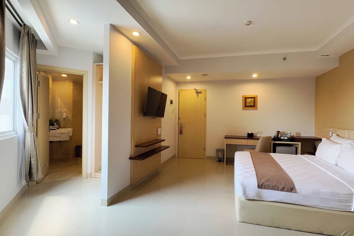 A hotel room with a bed, a desk, a TV, and a bathroom visible through an open door.