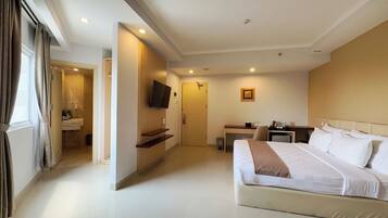 A hotel room with a bed, a desk, a TV, and a bathroom visible through an open door.