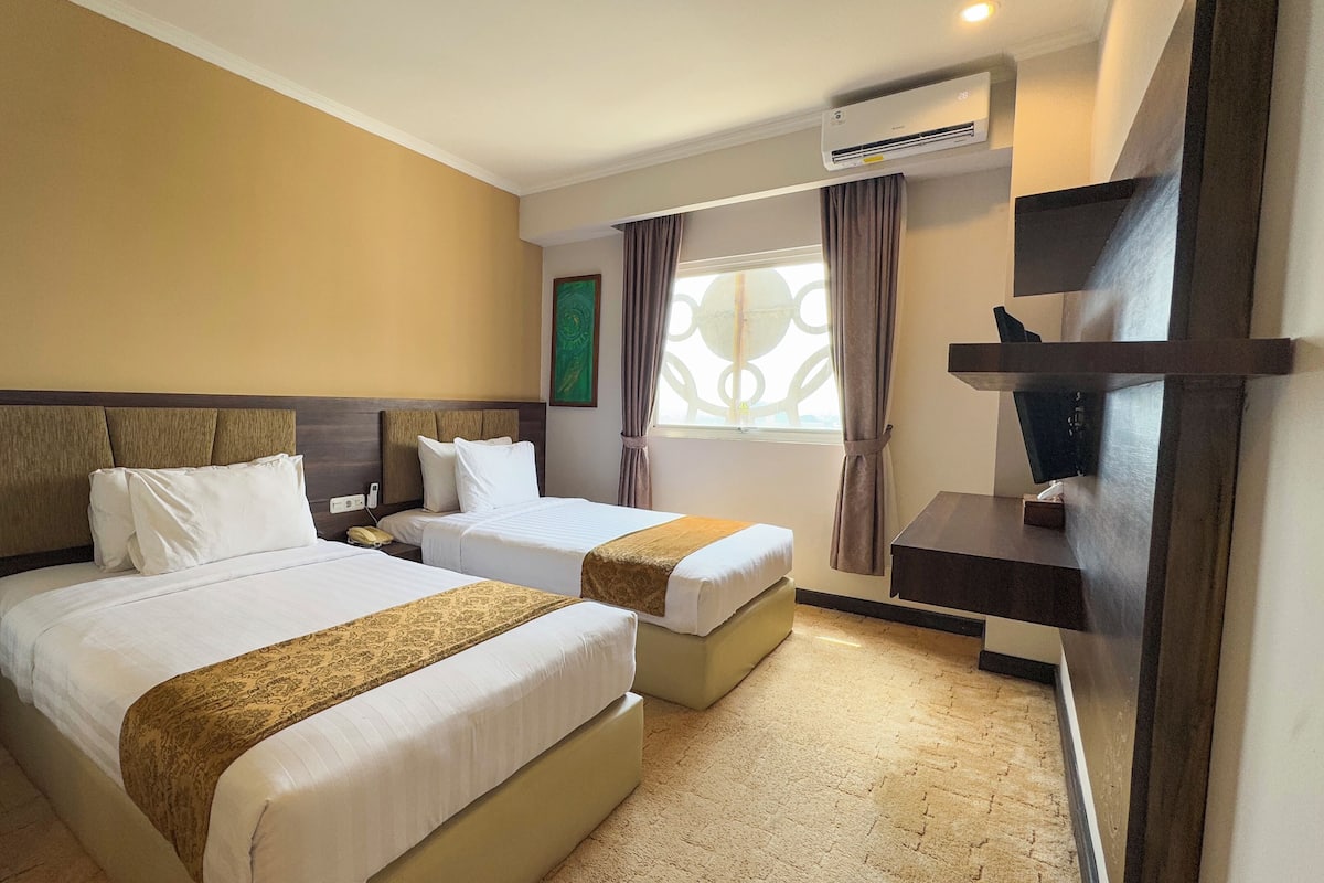 A hotel room with two beds, a TV, and an air conditioning unit.