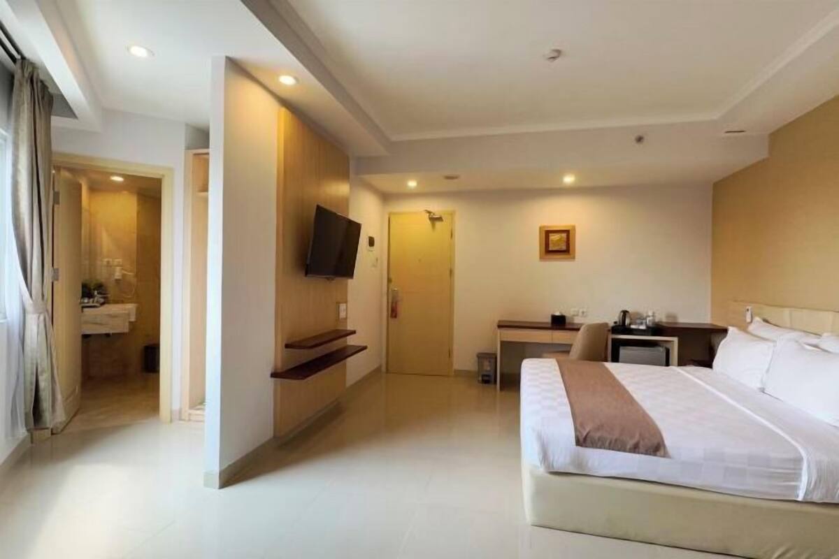 Ein Hotelzimmer mit Bett, Schreibtisch, Fernseher und einem durchgegangenen Badezimmer.