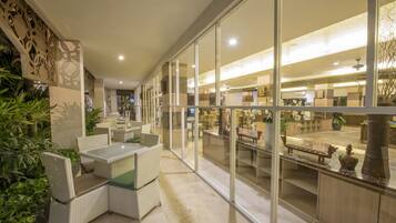 A spacious indoor area with a glass partition, wicker furniture, and indoor plants.
