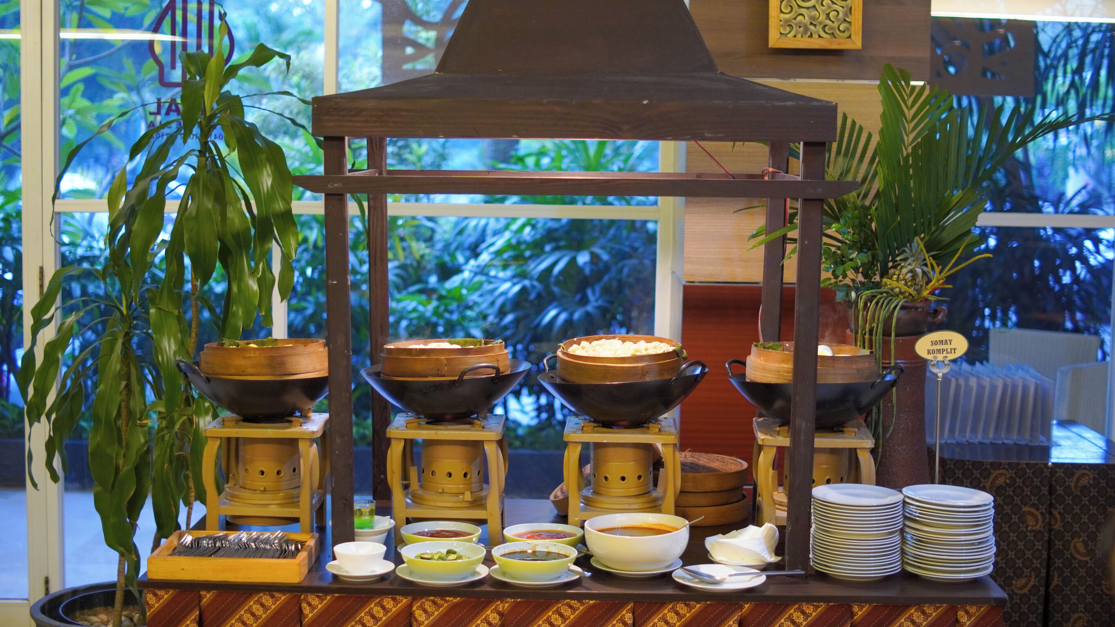 A traditional food display with various bowls and plates, a wooden structure, and a view of greenery through the window.