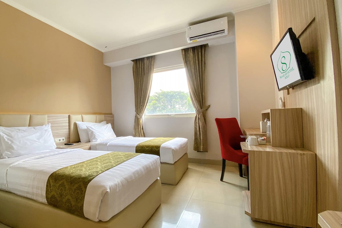 A hotel room with two beds, a desk, a chair, an air conditioning unit, and a TV mounted on the wall.