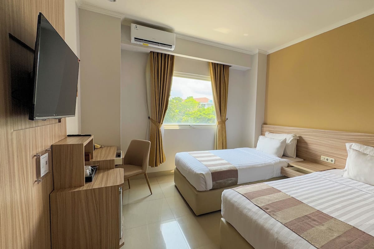 A hotel room with a bed, bedside tables, a TV, a desk, a chair, an air conditioning unit, and a window with curtains.