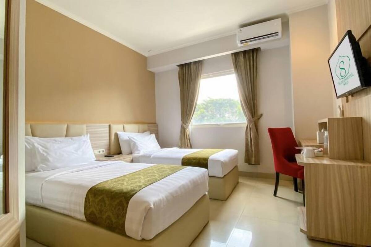 Ein Hotelzimmer mit zwei Betten, einem Schreibtisch, einem Stuhl und einer Klimaanlage.