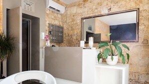 A reception area with a stone wall, a large mirror, a white reception desk, and a potted plant. - Hôtel Notre Dame (Bordeaux)