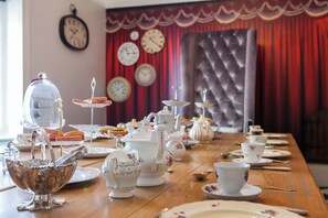Una mesa de comedor con varios conjuntos de té, teteras y tazas, con un reloj y cortinas al fondo.