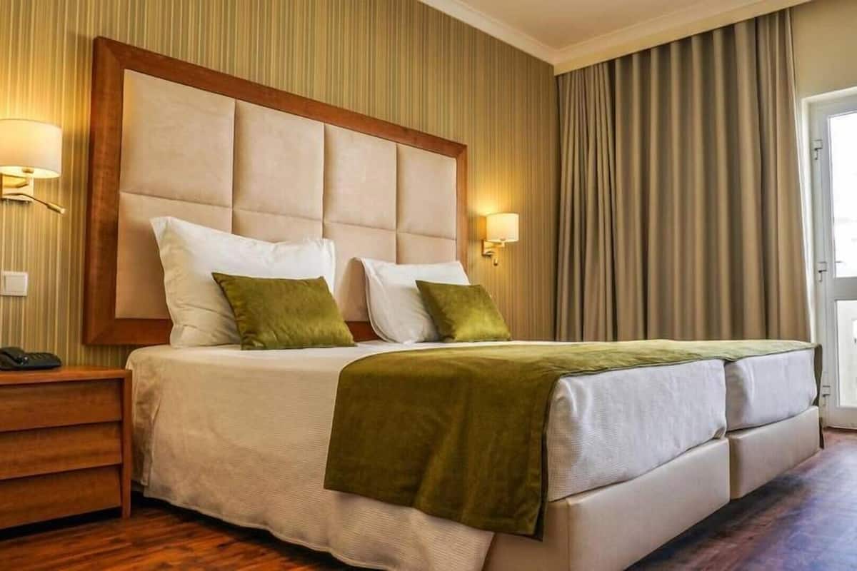Une chambre d’hôtel avec un grand lit, deux lampes de chevet, une table de chevet en bois et une vue sur l’extérieur par une porte.