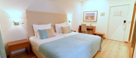 A hotel room with a bed, bedside tables, a desk, and a chair.