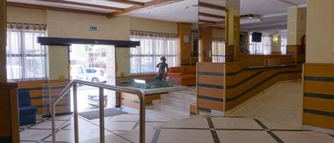 A hotel lobby with a staircase, a reception desk, and a statue.