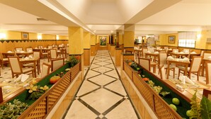 A hotel dining area with a central aisle, wooden furniture, and decorative plants. - Baía Beach Hotel (Vila Real Santo Antonio)