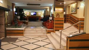 A hotel lobby with a marble staircase, red sofas, and a television in the background. - Baía Beach Hotel (Vila Real Santo Antonio)
