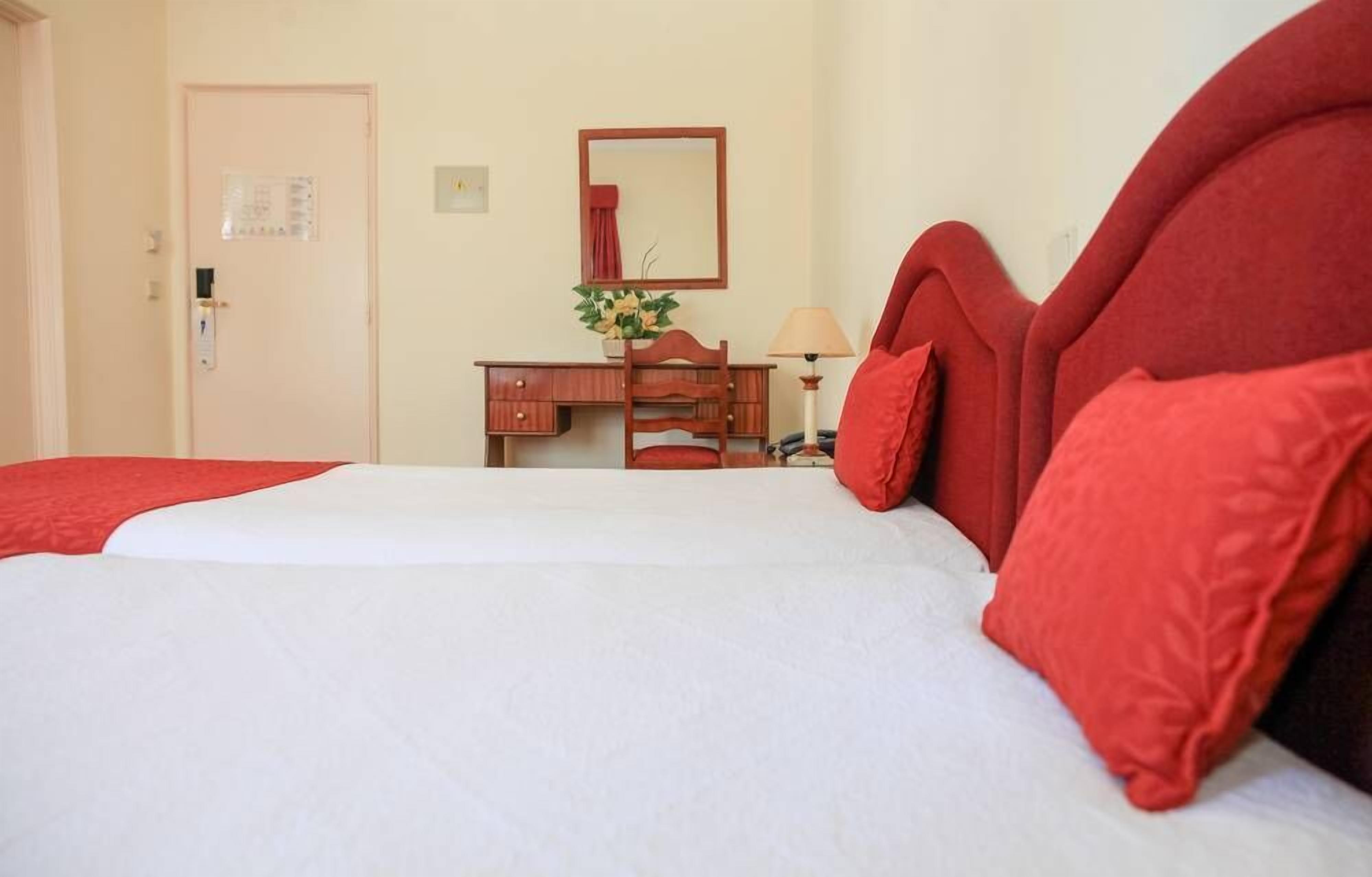 Ein Hotelzimmer mit Bett, einem Holzschrank, einem Spiegel und einer Lampe.