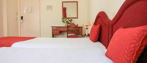 A hotel room with a bed, a wooden dresser, a mirror, and a lamp.