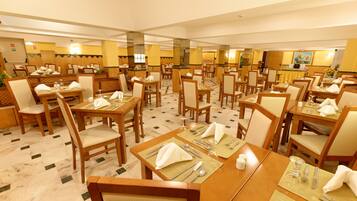 Un comedor de hotel con varias mesas dispuestas para comer, cada una con sillas, vajilla y una isla central con mostrador y sillas.