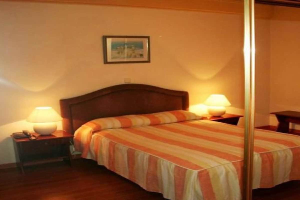 Une chambre d’hôtel avec un lit, deux lampes de chevet, une table de chevet et une petite table.