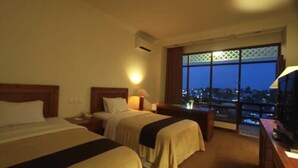 Habitación de hotel con dos camas, un televisor y un ventanal grande con vistas a la ciudad.
